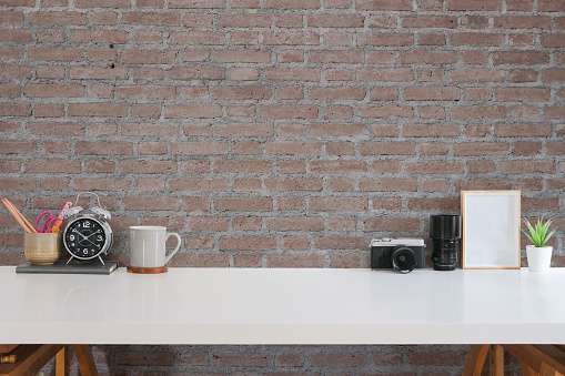 Creative workplace with camera, coffee cup, picture frame and stationery on white table.