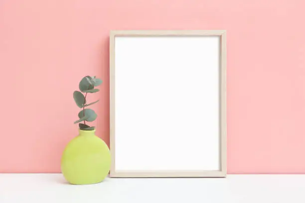 Mockup of a thin wooden frame with a sprig of eucalyptus. A stylized image of a thin vertical frame on a table. Minimalistic frame layout.