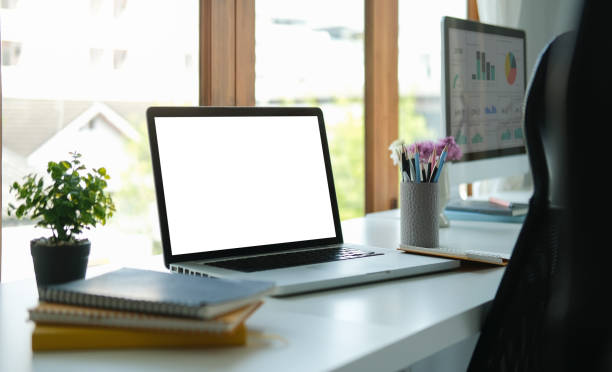 istock Computer laptop with empty screen, notebook and potted plant on white office desk. 1396806444