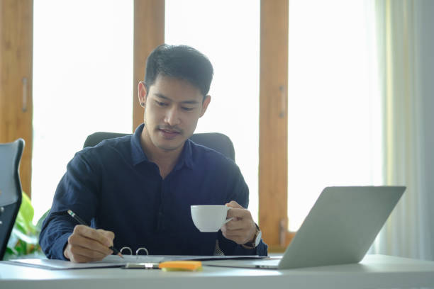 istock Successful young businessman drinking coffee and checking financial reports at office desk. 1396806472