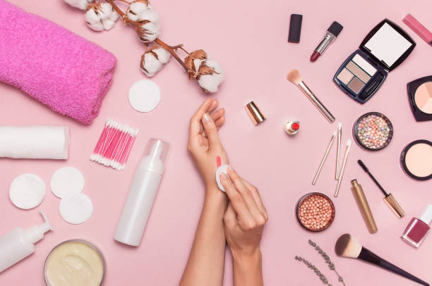 istock Make-up Remover Accessories. Flat lay background Womens hands try cosmetics, cotton branch, cotton pads, cosmetic bottle containers, pink towel, various make-up cosmetics, mascara, powder, lipstick. 1396809137