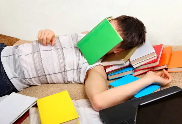 Tired Teenager sleeping on the Sofa with the Books
