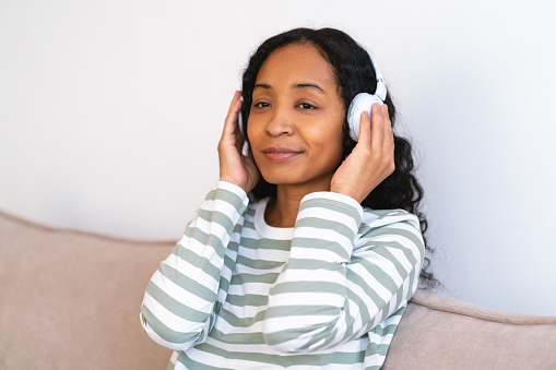 Having fun listening to music in earphones. Happy african-american woman having rest on sofa. Enjoying in free time at home. Entertaining yourself in spare time. Relaxing and chilling