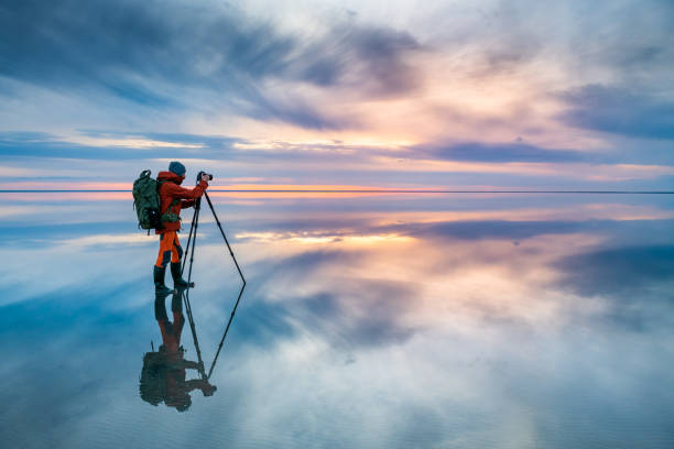 Photographer traveler taking photo of the beautiful lake at sunset. Photographer traveler taking photo of the salt lake at sunset. Blue sky with clouds are reflected in the mirror water surface. Professional photographer using tripod and dslr camera photographer stock pictures, royalty-free photos & images