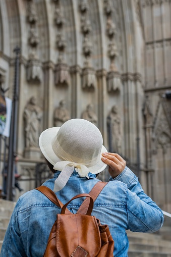 Unrecognizable tourist holding a hat on his back at the door of the Cathedral of Barcelona (Spain), travel concept.