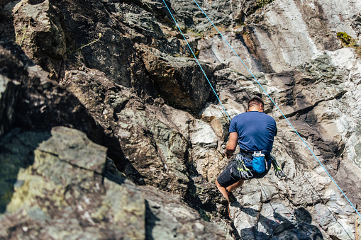 Adult man going down the rock, using a climbing rope.