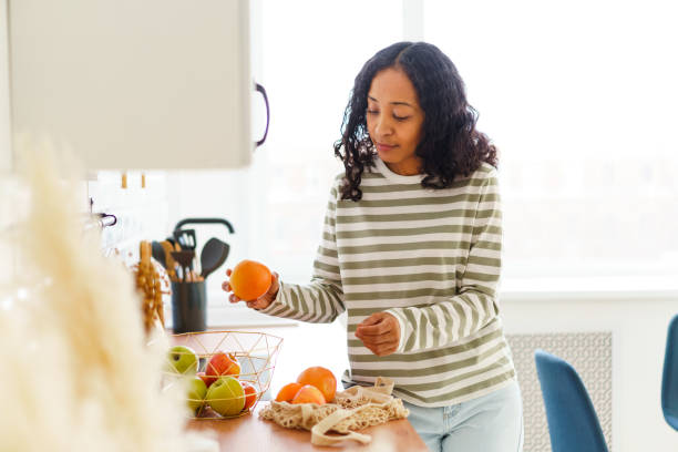 mujer afroamericana en la cocina clasificando manzanas y naranjas después de comprar en la tienda de comestibles - ripening process fotografías e imágenes de stock