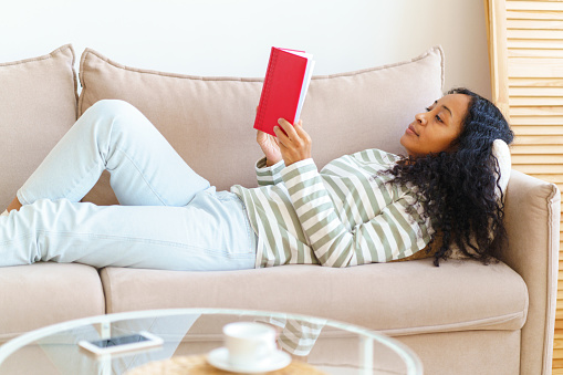 teenager reading book while sitting on couch at home