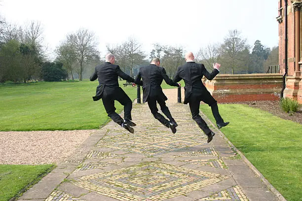 Bridegroom, best man and an usher jumping for joy. It could also be three businessmen.