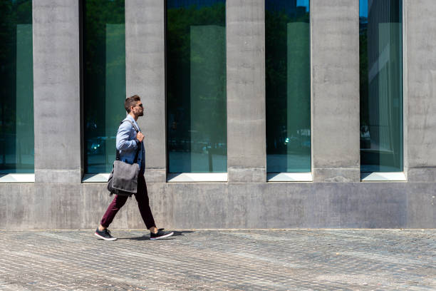 giovane uomo d'affari urbano professionista che cammina in strada indossando una giacca casual elegante. - borsa monospalla foto e immagini stock