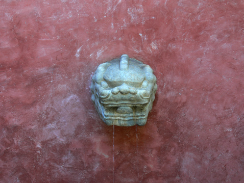 An asian inspired lion head wall fountain that is carved out of solid granite.