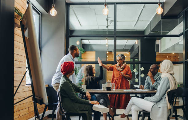 Successful businesswomen celebrating their achievement in an office Successful businesswomen high fiving each other during an office meeting. Two cheerful businesswomen celebrating their achievement. Happy businesspeople working as a team in a multicultural workplace. multiracial group stock pictures, royalty-free photos & images