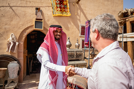 Mature global traveller in western attire shaking hands with young local salesman as he explores the town and its commercial opportunities.