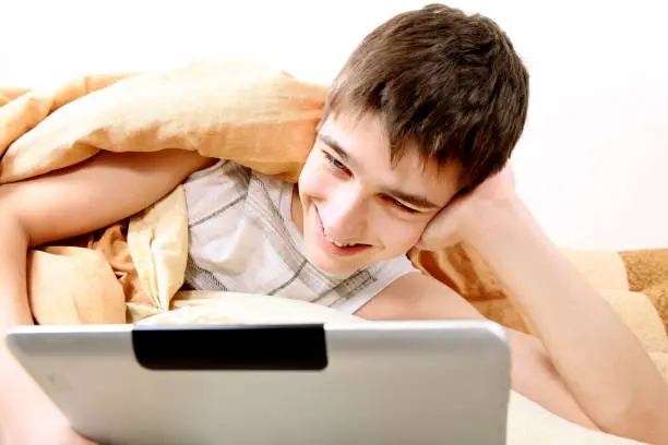 Cheerful Teenager with Tablet Computer in the Bed at the Home