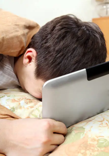 Sad Teenager Weeps with Tablet Computer in the Bed at the Home