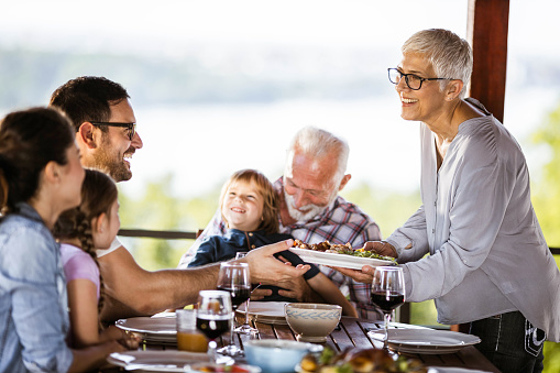 Happy extended family enjoying in lunch time on a balcony. Senior woman is serving food.