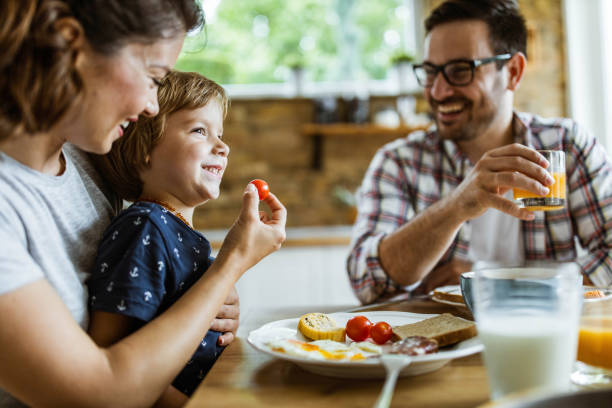 istock Small boy being fed by his mother during breakfast at dining table. 1396822354