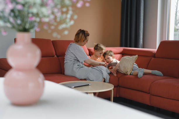 istock Mother reading book with two children on sofa 1396822898