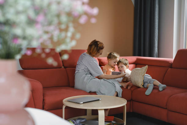 istock Mother reading book with two children on sofa 1396822900