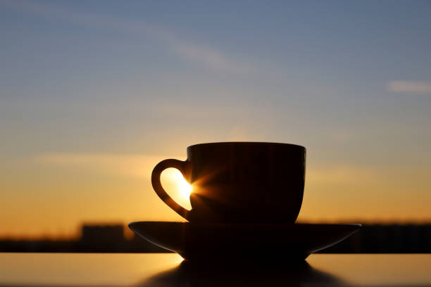 Black silhouette of coffee or tea cup on sunset sky background stock photo
