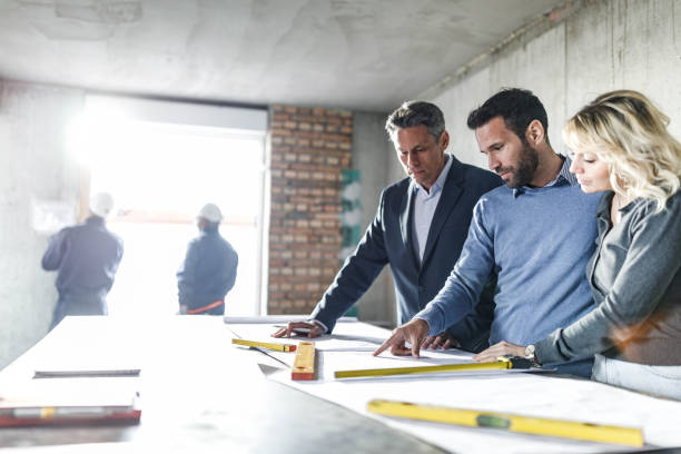 istock Young couple and their agent examining blueprints at construction site. 1396823001