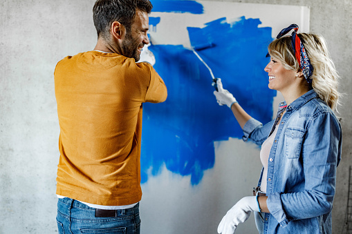 Happy couple communicating while painting their apartment during home renovation process.