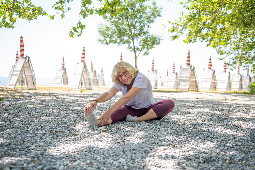 Senior woman doing yoga outdoors at the beach under beautiful trees, Adriatic sea, Italy.