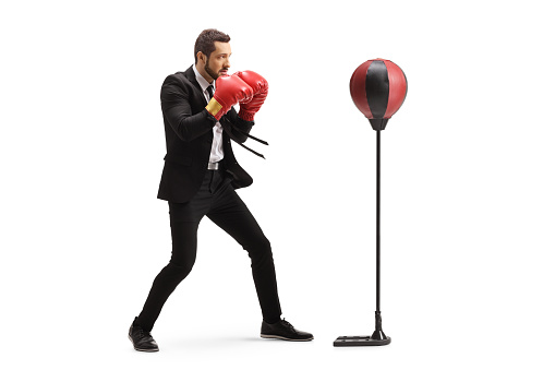 Full length profile shot of a man in a suit with boxing gloves training with a punch stand isolated on white background