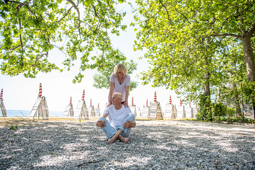 Seniors doing yoga outdoors on the beach under the beautiful trees. Adriatic sea, Italy,