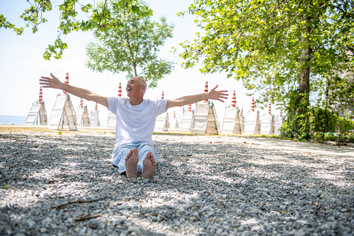 Senior man doing yoga outdoors at the beach under beautiful trees, Adriatic sea, Italy.