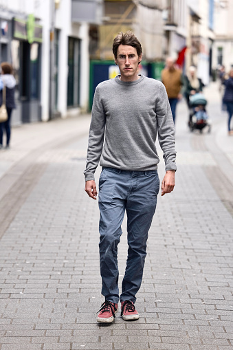 Man wearing a gray pullover walking in a quiet town centre.