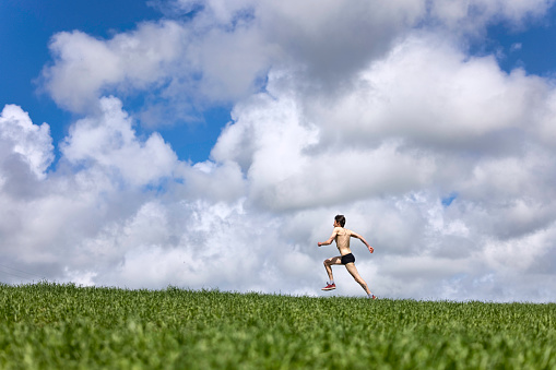 Long distance runner out in the countryside running across a field.