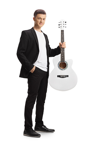Full length portrait of an elegant young man in a black suit holding an acoustic guitar isolated on white background