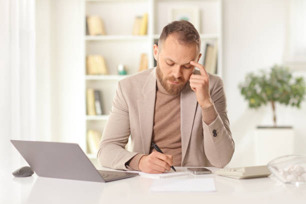 istock Man writing on a paper at home with a laptop computer 1396831425