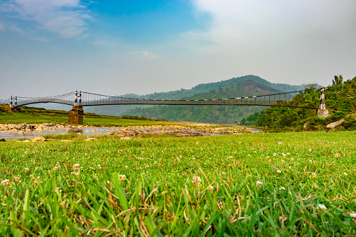 isolated iron suspension bridge over flowing river with mountain and blue sky background at morning image is taken at nongjrong meghalaya india.