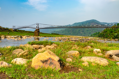 isolated iron suspension bridge over flowing river with mountain and blue sky background at morning image is taken at nongjrong meghalaya india.