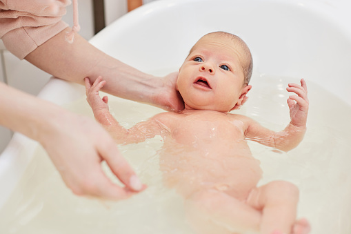 first bath of a newborn, mother bathes her cute beautiful baby in a white small plastic tub