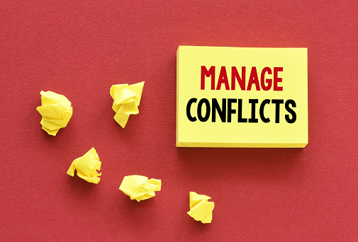 MANAGE CONFLICTS words on a small yellow piece of paper.