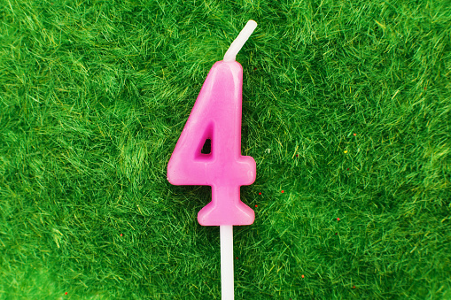 candle in the form of number four on the green grass background, a place for a greeting text