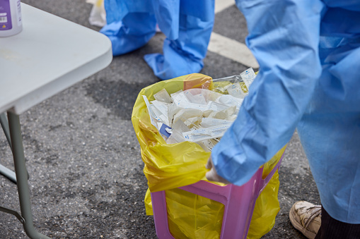 A medical worker in protective suit is managing disposal yellow trash bag for infectious waste.