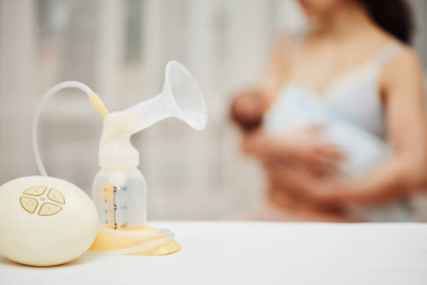 breast pump with breast milk against the background of a mother holding child. stock photo