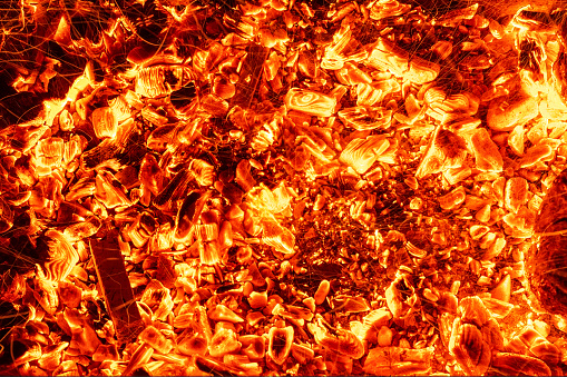 Top above overhead detail view od abstract hot red burning wooden coal background in bbq grill brazier or firepit at dark night time. Beautiful inferno heat sparks glowing flaming at hearth stove.