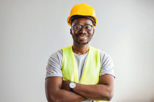 Happy African Builder Workman Standing Pleased Happy African Builder Workman Standing Pleased Crossing Hands Posing On Gray Studio Background. Copy Space.  Industrial engineer industrial labourer stock pictures, royalty-free photos & images