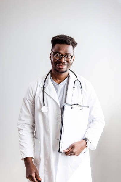 Portrait of happy african doctor at private clinic Portrait of happy african doctor at private clinic. Happy african american male nurse. Friendly african male therapist posing over gray background. Medical concept of young male doctor in white coat with phonendoscope, waist up. biochemist stock pictures, royalty-free photos & images