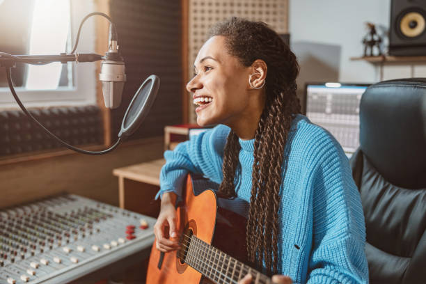 istock Pleasant cute multiethnic woman singing into microphone and playing guitar in the broadcasting of sound recording studio 1396841765
