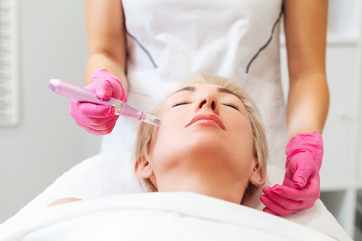 Professional beautician in medical pink gloves does mesotherapy on the cheek of a beautiful caucasian woman. The concept of aesthetic medicine and hardware cosmetology.