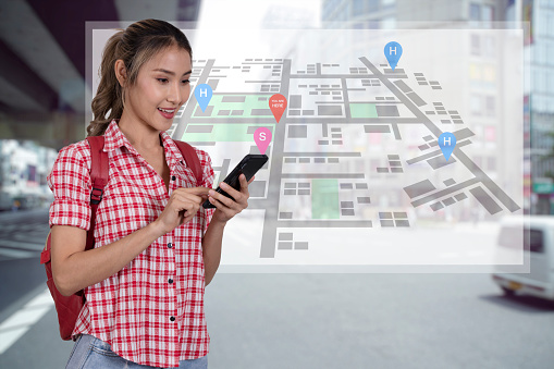 Tourist woman use gps navigation application on smartphone to search place to visit. Tourist woman in red plaid shirt and backpack holding smartphone with location map screen on background.
