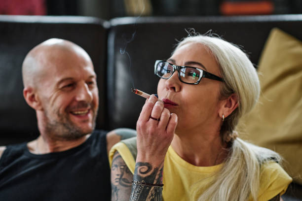 Mature Woman Smoking Weed Selective focus shot of mature Caucasian woman with long gray hair and tattoos on arm smoking cannabis cigarette marijuana tattoo stock pictures, royalty-free photos & images