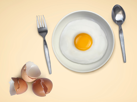 spoon fork fried egg on plate on a Cream background