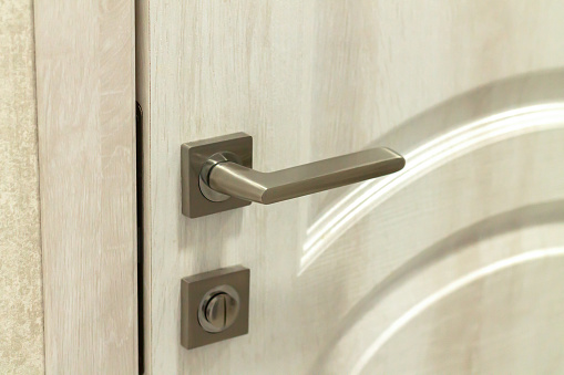 Metal door handle or doorknob with security lock on wooden background
